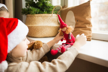 Fototapeta na wymiar child plays with doll on windowsill against background of Christmas tree