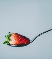 Vertical shot of a tasty strawberry placed on a spoon isolated on a light blue background