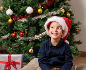 Little boy wearing santa hat smiling looking to the side and staring away thinking.