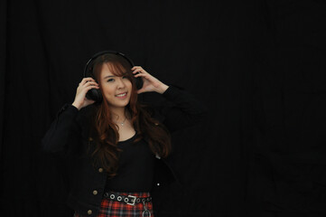 portrait young asian female singer wearing  headphones, attractive cheerful girl standing isolated on black background .soft focus