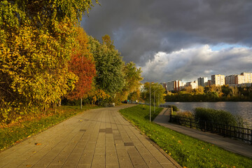 Sidewalk in autumn city park with waterfront and dramatic sky with clouds