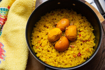 Uma panela preta com arroz e pequi sobre uma tábua de madeira e um pano de prato. Um prato típico brasileiro.