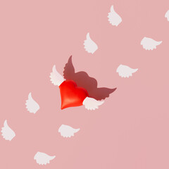 Red heart with white wings, creative love inspired layout against pastel pink background. 