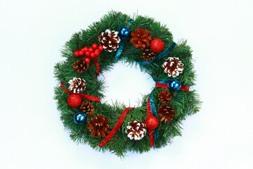 Fototapeta na wymiar Top view of a bright beautiful Christmas wreath decorated with cones, red and blue Christmas balls, shiny ribbons. Wreath on white background, New Year and Christmas concept