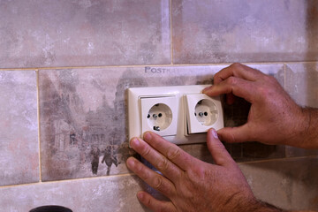 A worker repairs a socket in a wall.