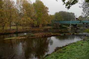 Obraz premium Scenic view of a bridge over a river during autumn on a cloudy day