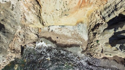 Aerial tp view of a sea surrounded by cliff formation on a sunny day in Greece
