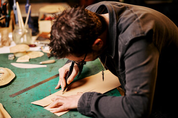 Portrait of leather craftsman cuts leather with a scalpel at table in workshop studio