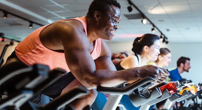 African man and friends exercising on fitness bike in gym