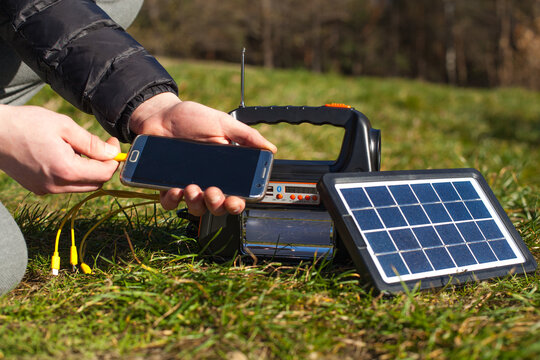 A man puts a solar-charged phone on the charger. Portable power station on ecological energy for hiking, tourism and travel.