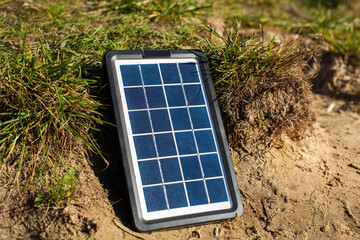 A solar panel stands on a background of sand and green grass. The sun floods the solar panel with...