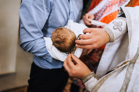 A male Christian priest in a church conducts a sacred rite, a ritual for a newborn child, cutting off the hair on his head with scissors. Photography, religion.