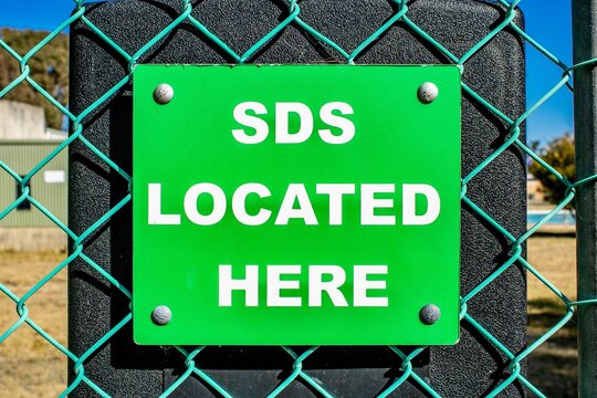 Closeup of green square SDS LOCATED HERE sign on turquoise mesh wire fence against black surface
