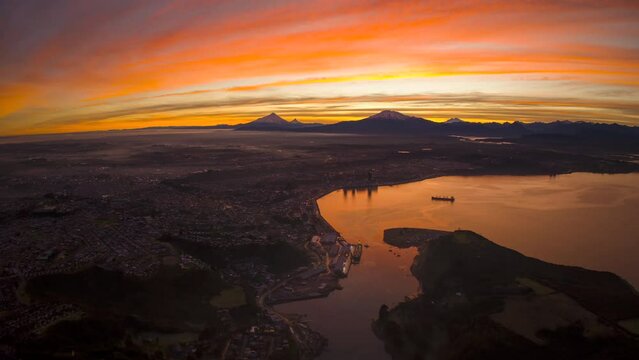 Aerial hyper-lapse of colorful sunrise clouds moving over lakeside Puerto Montt city in Chile