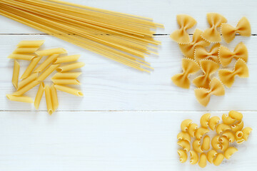 Maccheroni raw, mixed, on white wooden board background, top view, space to copy text..