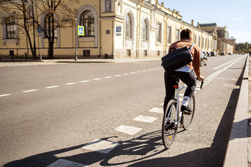 A male cyclist rides to work with a briefcase on a bicycle in the city. Ecological transport is modern.