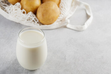 Potato milk and raw potatoes in a mesh bag. Alternative non dairy drink and ingredients on gray background. Allergens free and zero waste concept. Top view. Copy space