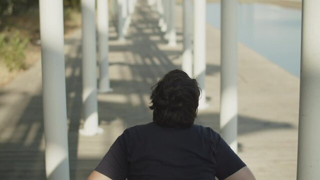 Rear view of woman using wheelchair walking down street. Young Caucasian woman wheeling along alley of pylons in park. Woman with disability concept