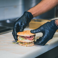 Hamburger style big mac tenu par un employé de fast food avec des gants noir