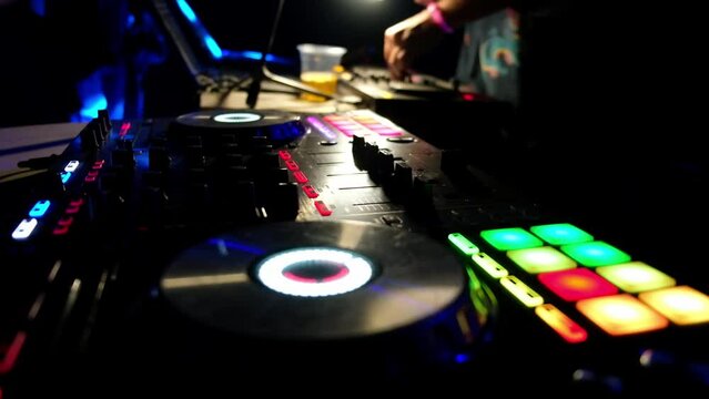 DJ playing music at party. Shimmering with different colors pads of music beat sampler at foreground. Digital audio beatmaking machine. DJ audio equipment