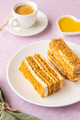 Dessert, sliced layered honey cake with cream on a white plate on a pink concrete background. Valentine's day concept.