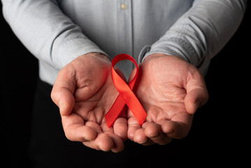 A man showing his two open hands holding a red ribbon in support of World AIDS Day. Understanding and empathy for hiv patients - obrazy, fototapety, plakaty