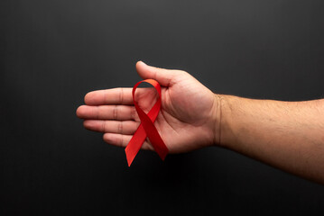 The open palm of a man holding a red ribbon for World AIDS Day, on a black background