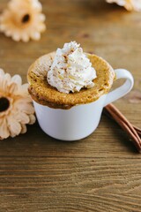 Vertical shot of an appetizing Pumpkin Spice Mug Cake surrounded by flowers and cinnamon rolls