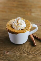 Vertical shot of an appetizing Pumpkin Spice Mug Cake surrounded by cinnamon rolls on the table