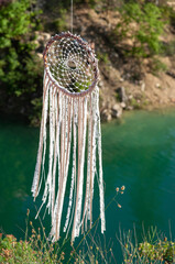 Close up dream catcher hanging over the azure lake, bohemian craft outdoors