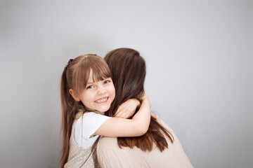 Fototapeta premium Young mom and her charming cute little daughter are hugging and smiling on a gray background. Concept for mother day