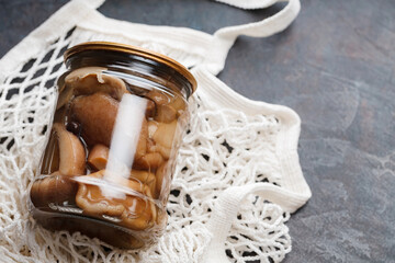 Pickled mushrooms in jar on a dark background. Canned mushrooms in a shopping bag. Copy space