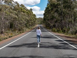 Young Australian woman walking on an asphalt road through the woods in sunny weather in Tasmania