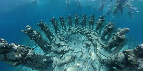 Underwater scenery with sunk old sculptures covered in moss and people scuba diving in Bali