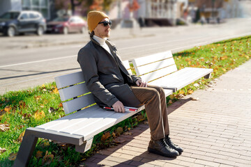 Blind man with a walking stick sitting on a bench in the city
