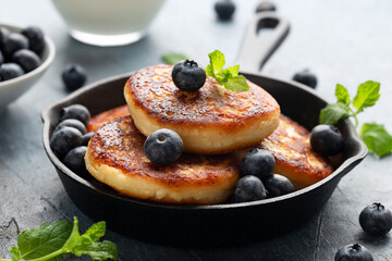 Cottage cheese pancakes served in cast iron frying pan with blueberries and mint leaves. Healthy breakfast food.