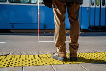 Close-up of a blind man with a cane stopped on a tactile tile in front of a tram obstacle