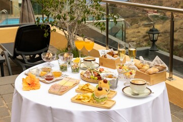 Top closeup of a round table outdoors with white tablecloth and burgers, chips, glasses of champagne