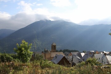 High-angle of Vilamos in Aran valley, misty, sunlit Pyrenees mountain range, cloudy sky background