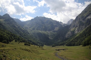 High-angle Aran valley with forested, misty, sunlit Pyrenees mountain range, cloudy sky background