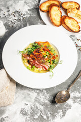 Pea soup. Delicious vegetable soup with green peas, carrots and fried bacon. Vertical shot. Copy space. Gray background