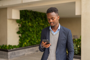 Portrait of handsome black African businessman texting with mobile phone