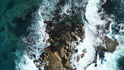 Obraz premium Aerial top view of huge rocks on ocean shore, turquoise strong waves hitting on stone