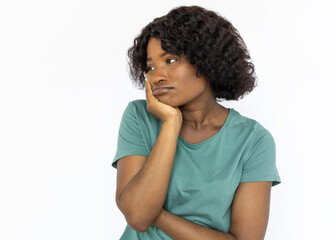 Bored young woman looking away and dreaming. Female African American model with curly hair in green T-shirt missing someone and thinking, holding hand on her cheek. Emotions, boredom concept