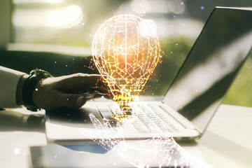 Creative idea concept with light bulb illustration and hands typing on laptop on background. Multiexposure