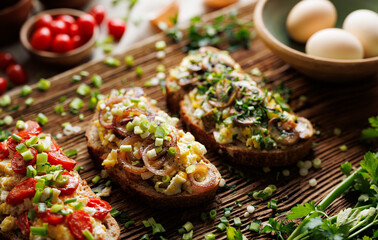 Sandwiches with scrambled eggs and various vegetables, focus on on the sandwich with onion rings  on a wooden plank