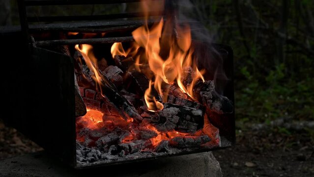 Camping fireplace with an active flickering fire in a bed of glowing coals.
