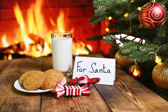 a glass of milk, a plate of oatmeal cookies and sweets on the background of a Christmas tree, a fireplace and a sign For Santa