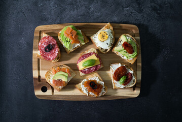 Variety of tapas sandwiches for aperetif on wooden on black background. Top view.