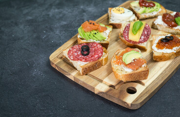 Variety of tapas sandwiches for aperetif on wooden on black background.